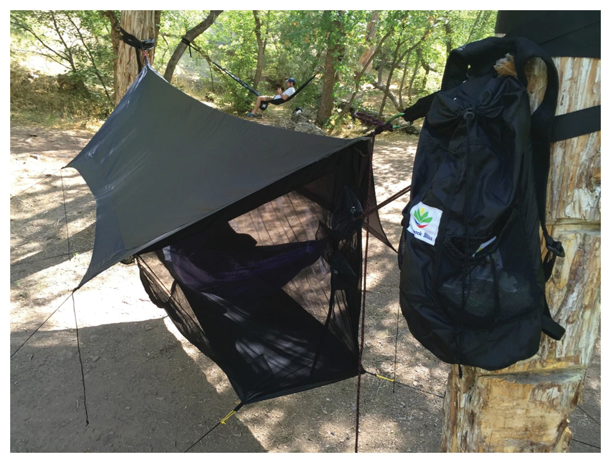 Black Hammock Bliss Sky Tent 2 suspended between trees with a backpack beside the shelter