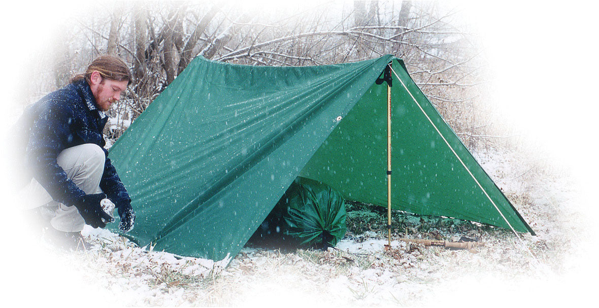 Camper beside a green Equinox Egret tarp shelter in the snow