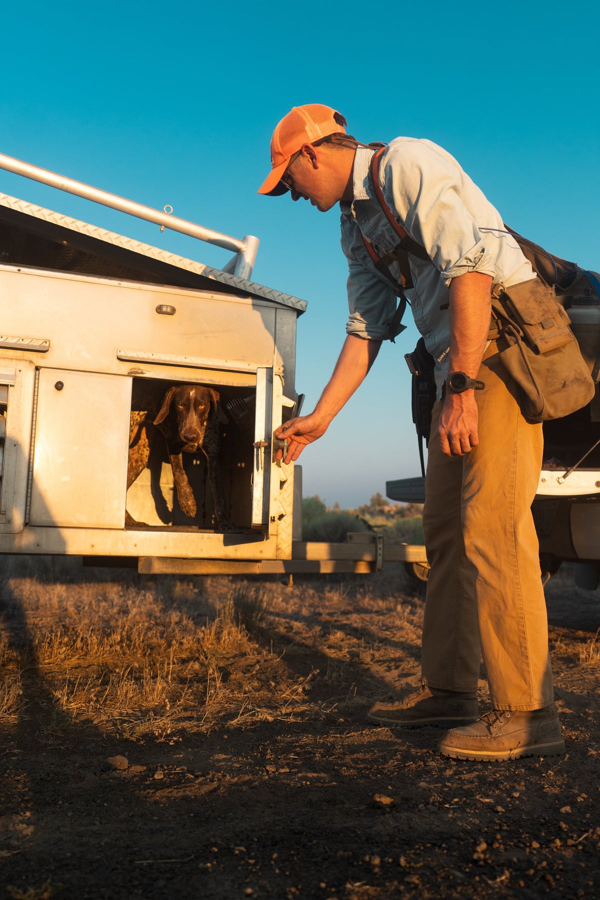 Handler standing beside a vehicle with dog equipment