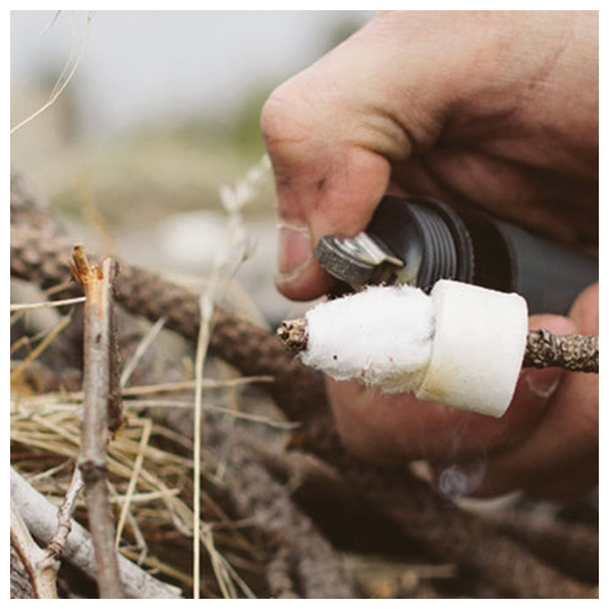 Hand using the Zippo flint spark wheel beside tinder on a small branch