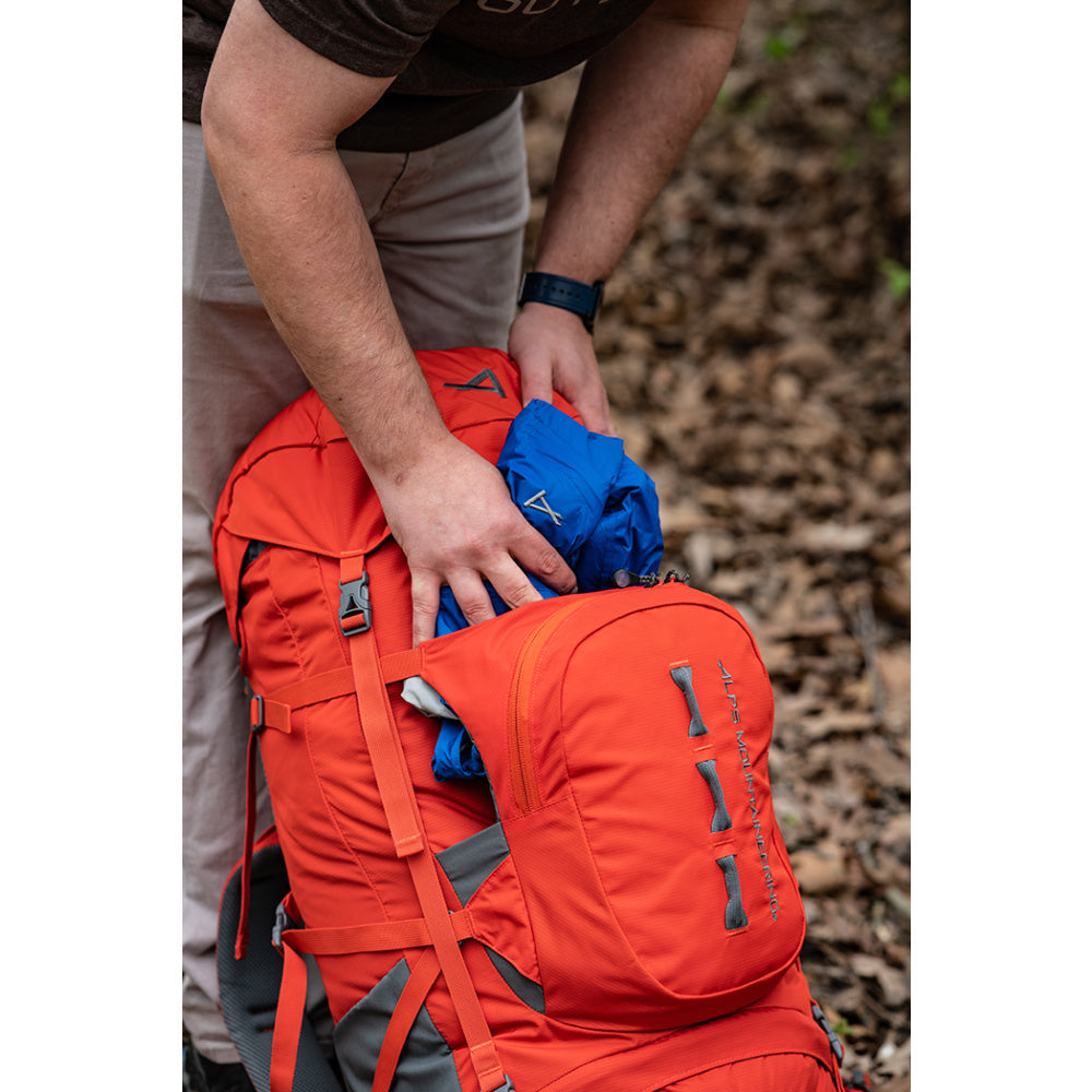 Hiker placing gear into the front kangaroo pocket of a Chili Red Tail 65L pack
