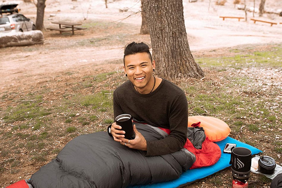 Camper sitting on a blue ALPS Flexcore pad at camp