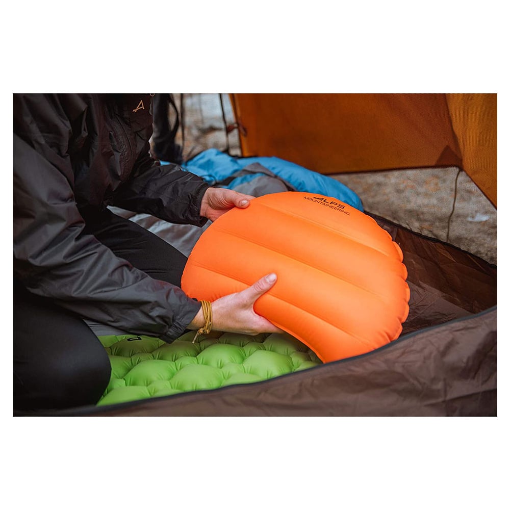 Camper holding an orange ALPS Versa pillow inside a tent