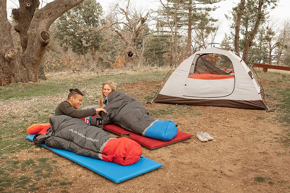 Campers using blue and red ALPS sleeping pads beside a tent