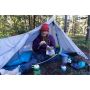 Camper seated outside a tent with camp-cooking equipment