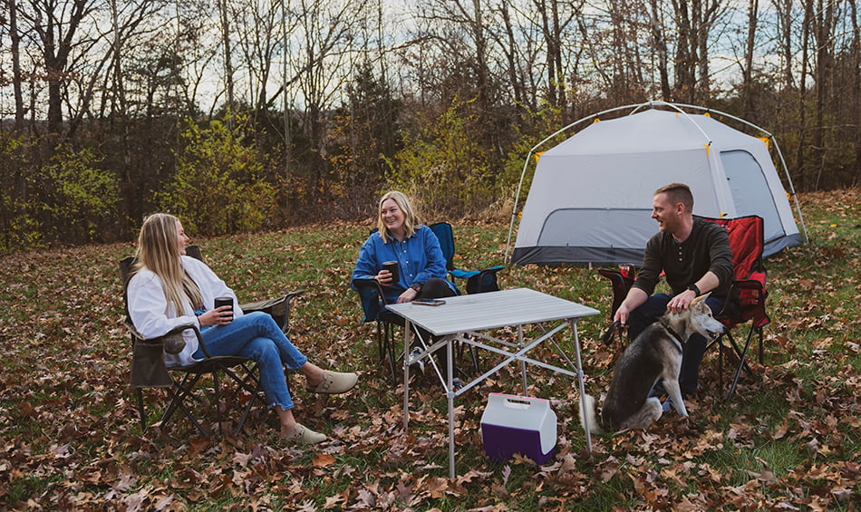 Campers seated around an ALPS Camp Table beside a tent
