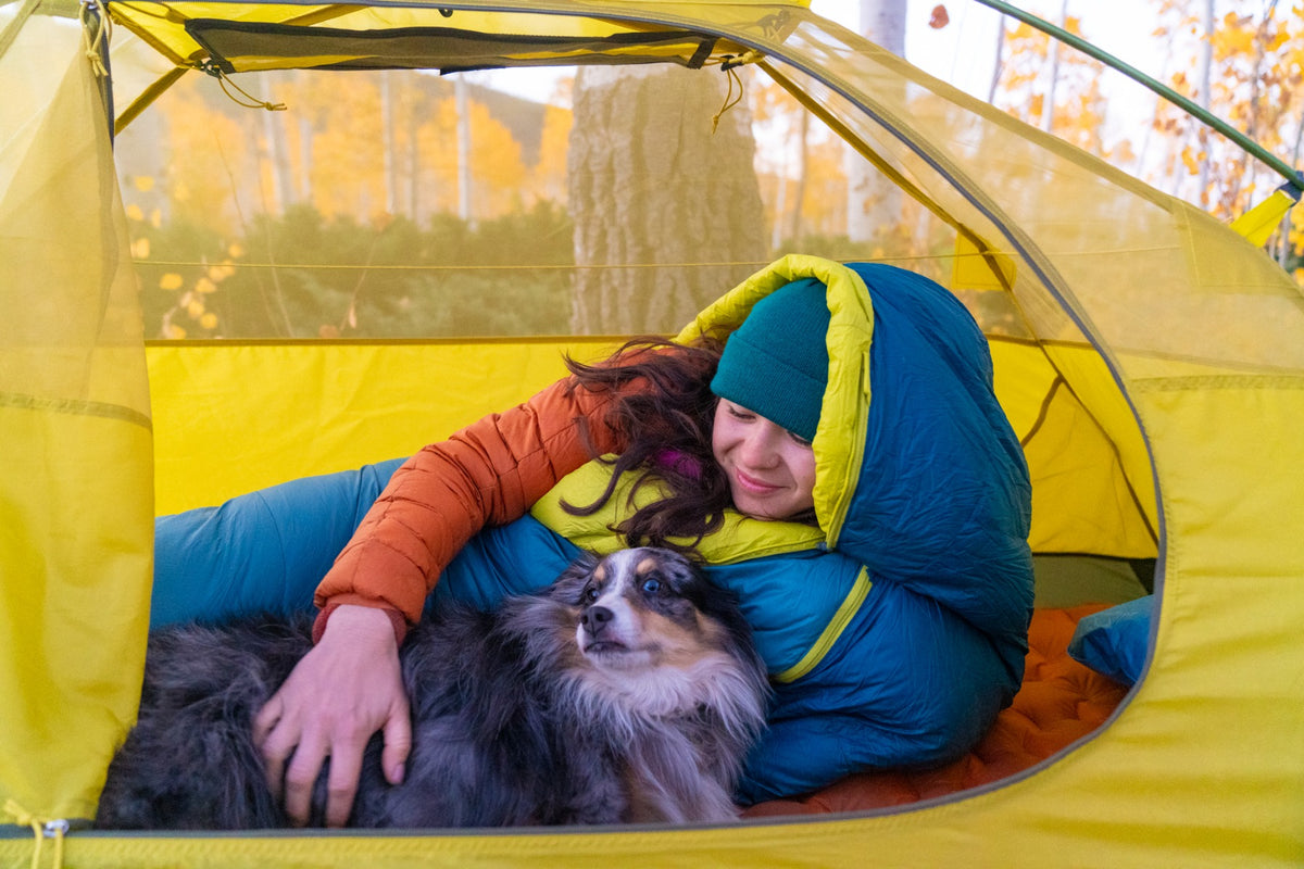 Camper and dog resting beside a Peregrine Anatum sleeping bag in a tent