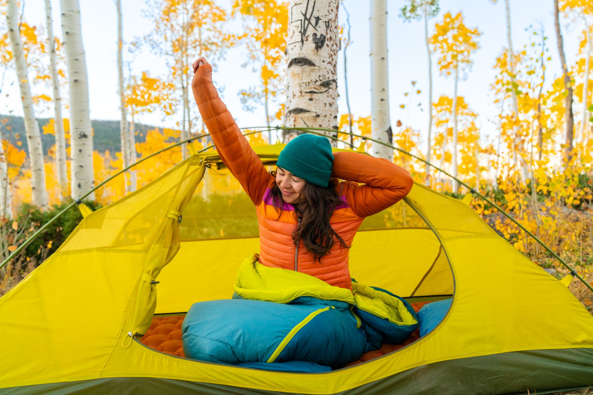 Camper sitting in a Peregrine Anatum sleeping bag inside a yellow tent