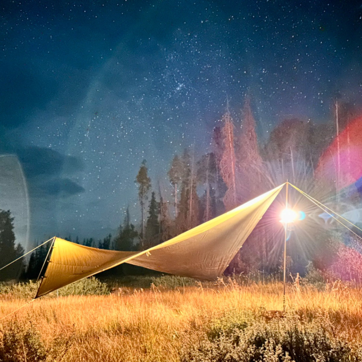 Peregrine Spanner tarp shelter illuminated at a nighttime campsite