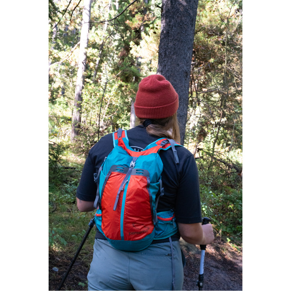 Hiker wearing a blue and orange Peregrine Vanga 25L pack on a wooded trail