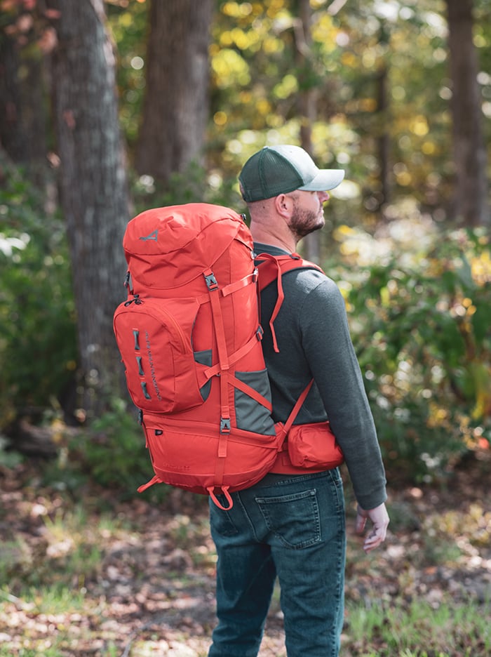 Hiker wearing a Chili Red Tail 65L pack, viewed from behind in the woods
