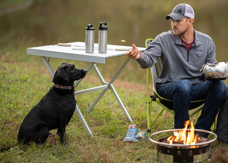 Silver ALPS Square Dining Table holding bottles beside a camper and dog
