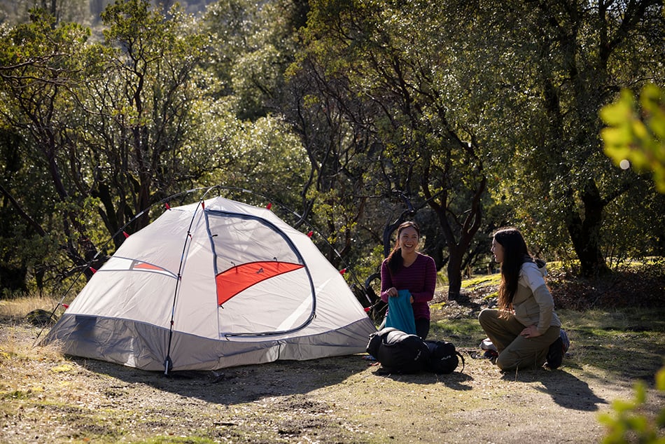 Two campers sitting beside an ALPS Taurus mesh tent body