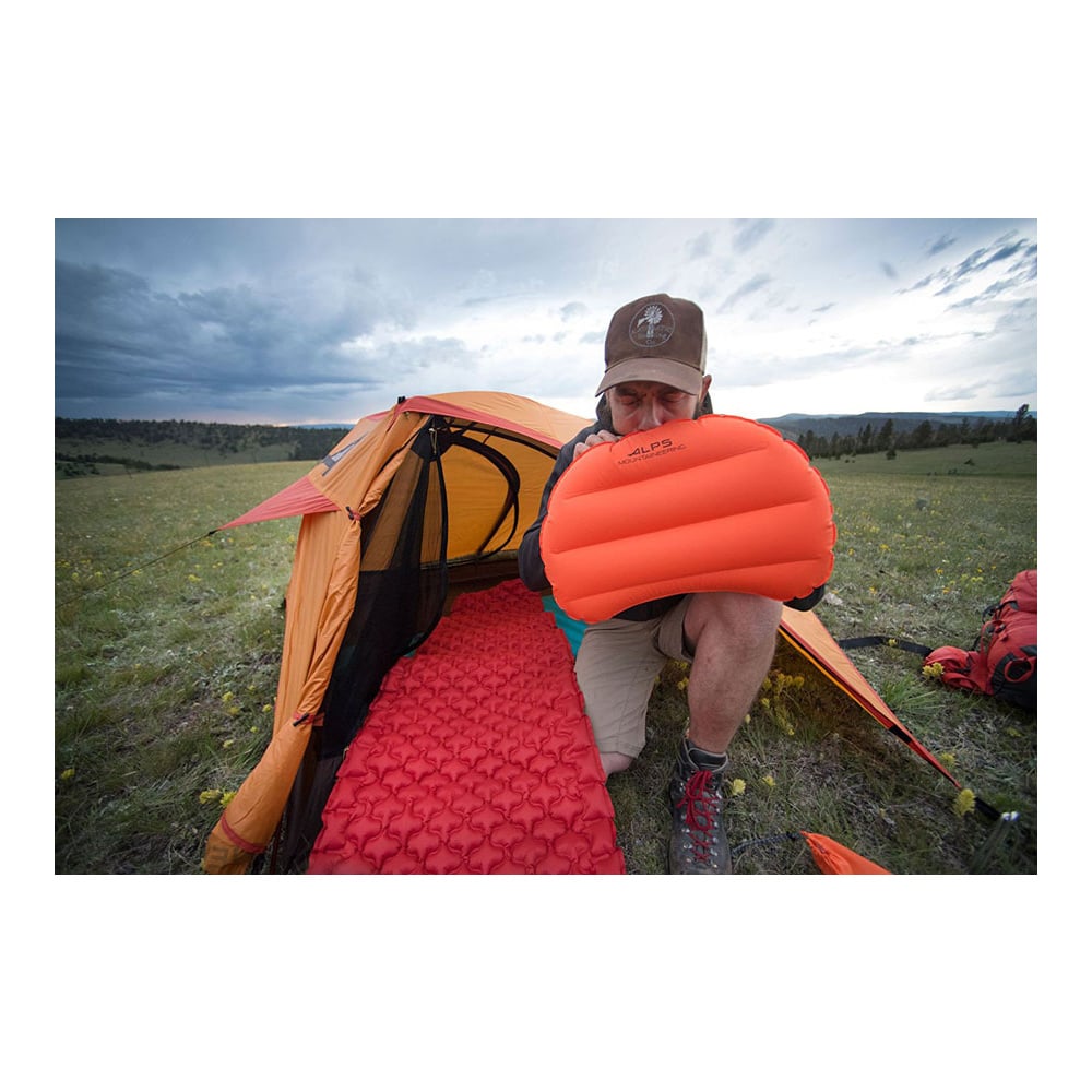 Camper holding an inflated orange ALPS Versa pillow outside a tent